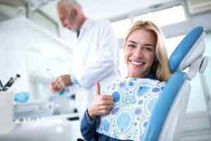 Girl on the dentist chair and showing positive sign and dentist standing near her