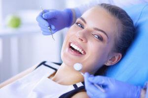 Girl on the dentist chair and showing positive sign and dentist standing near her