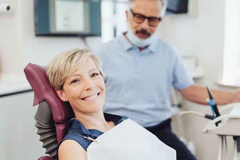 Girl on the dentist chair and showing positive sign and dentist standing near her