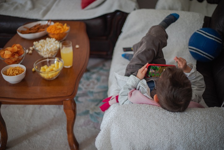 Screen time and snacking habits of a child with a smartphone and assorted snacks